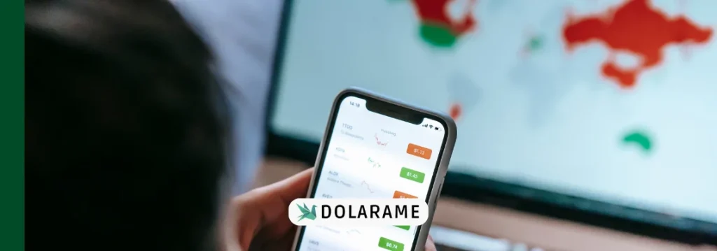 Pessoa segurando celular com gráficos de ações e atrás o mapa mundi para indicar as maiores bolsas de valores do mundo